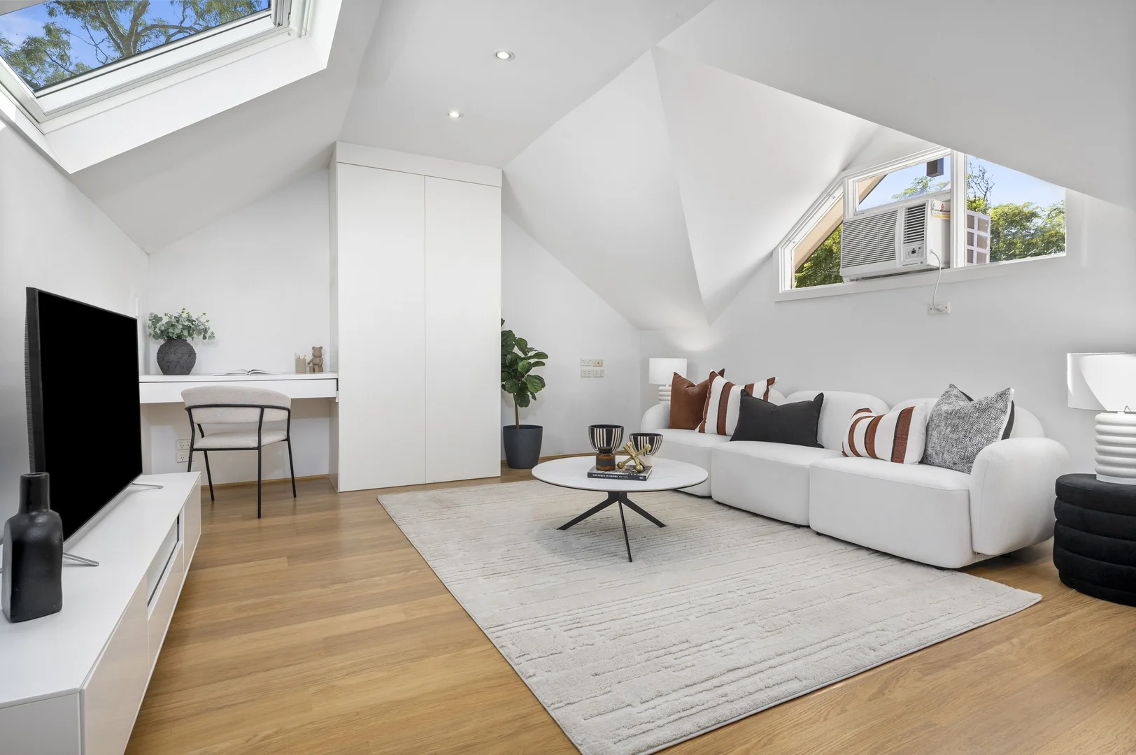 An attic-converted living room with a white modular sofa, black-and-rust pillows, and a small white coffee table.