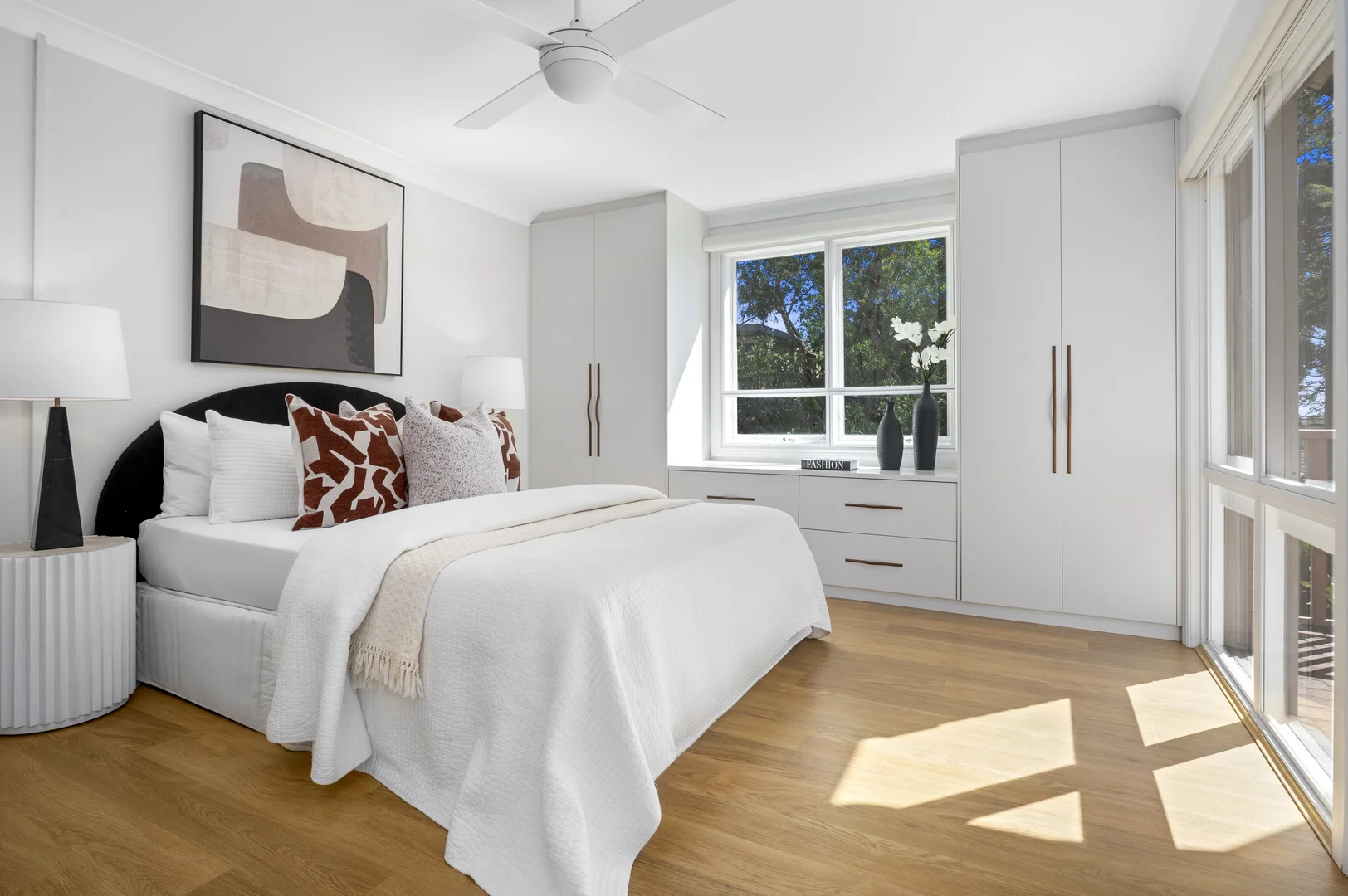 A plain bedroom with grey-and-rust pillows and an abstract artwork.