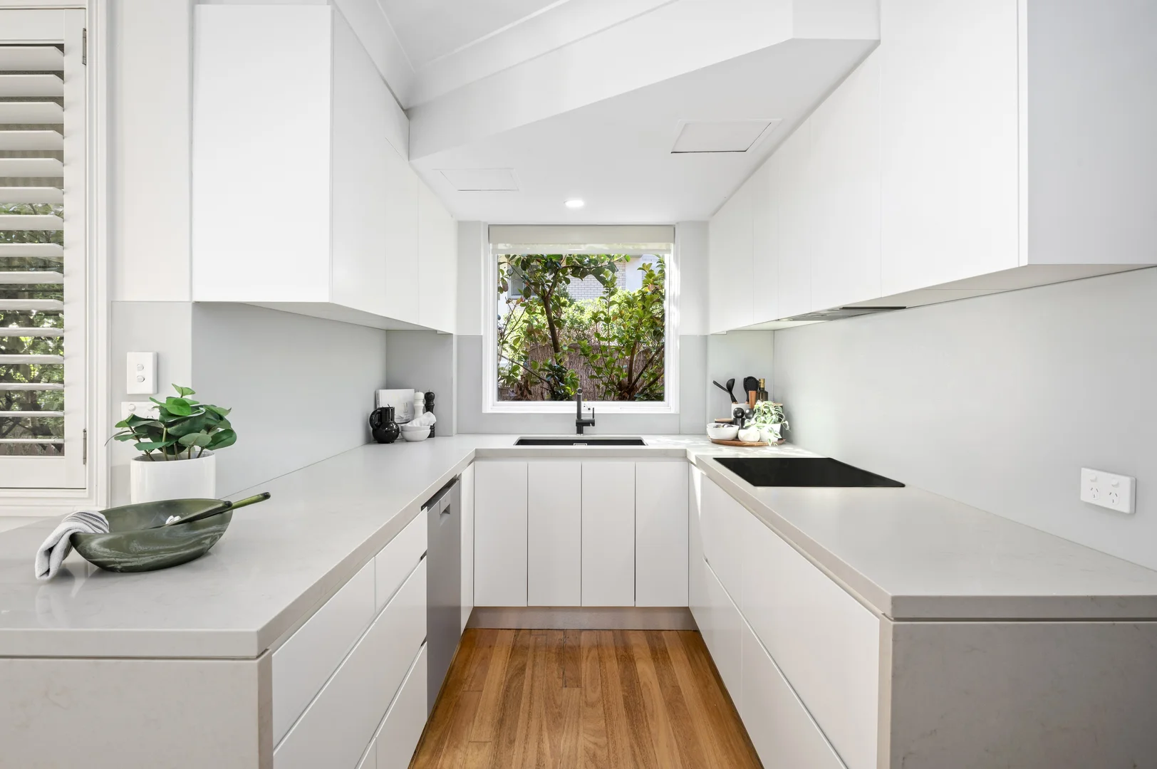 A bare U-shaped kitchen with stone benchtops and white cabinetry.