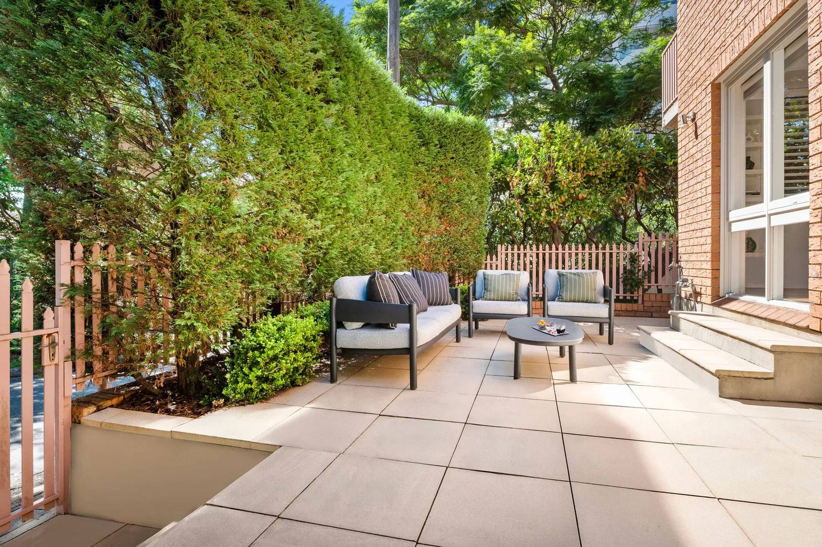 A blank concrete-paver patio with cool-grey outdoor furniture and a hedge.